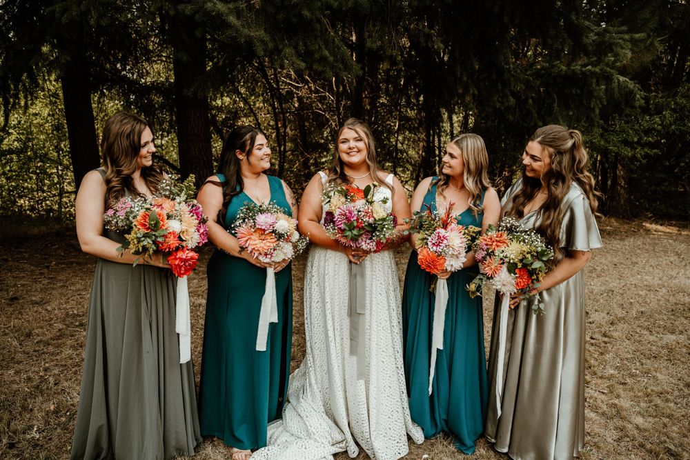 Bridesmaids in teal and gray dresses hold bouquets while standing outdoors.