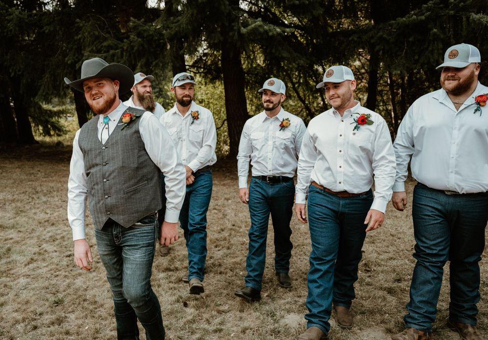 A group of groomsmen in western attire walking together outdoors wearing cowboy hats and blue jeans.