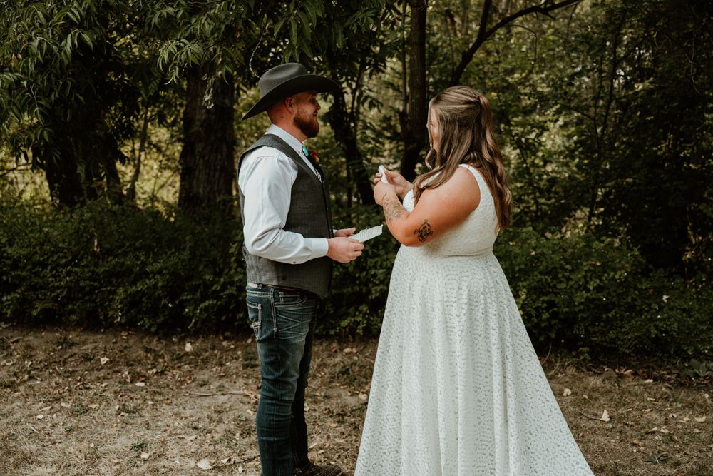 A couple in western wedding attire sharing a tender moment on a dirt path surrounded by trees.