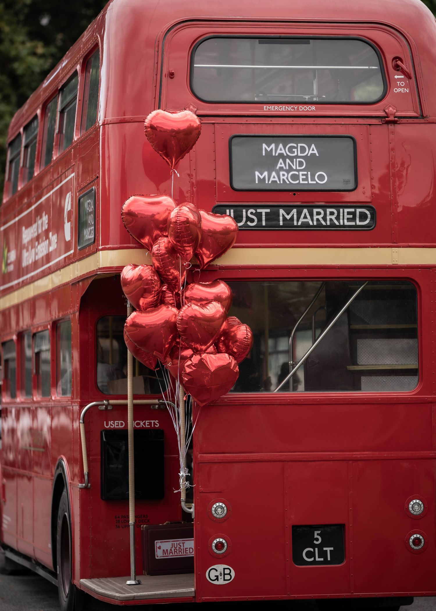 Red double-decker bus decorated with 'Just Married' sign and red heart-shaped balloons.