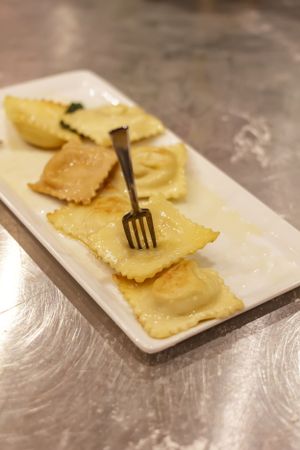 Fresh ravioli pasta arranged on white plate with decorative fork.