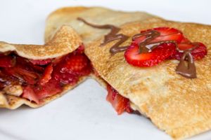 A crepe filled with fresh strawberries and chocolate drizzle cut in half to show the filling.