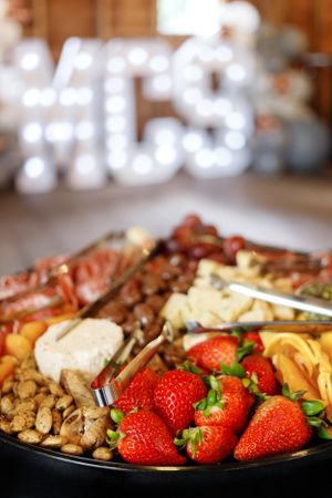 Party platter with fresh strawberries, meats, cheeses and nuts with illuminated sign in background.