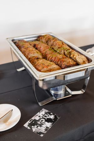 Grilled chicken breasts in chafer dish on black tablecloth.