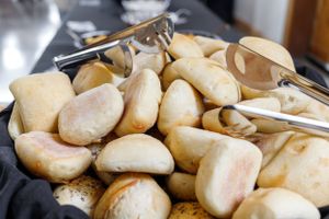 Fresh dinner rolls in silver serving tray with tongs.
