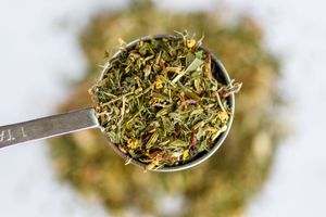 Close-up macro photo of dried green herbs with stems and leaves scattered on a wooden surface.