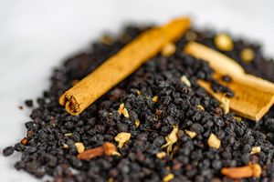 Close-up of black peppercorns scattered with cinnamon sticks on a white surface.