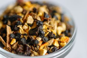Close up macro shot of dried loose leaf tea with black and golden organic pieces in a white ceramic bowl.