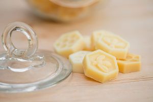 Close-up of honeycomb-shaped yellow candle melts next to a glass jar lid on wooden surface.
