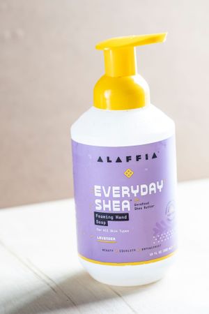 A bottle of Alaffia Everyday Shea foaming hand soap with purple and white packaging and yellow pump dispenser.