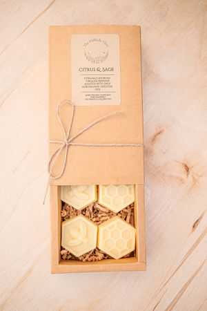 Kraft paper gift box with string tie containing honeycomb-shaped candle melts nestled in wood shavings.