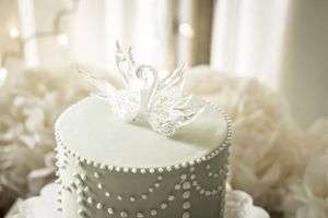 Elegant white wedding cake decorated with pearl details and crystal swan topper.