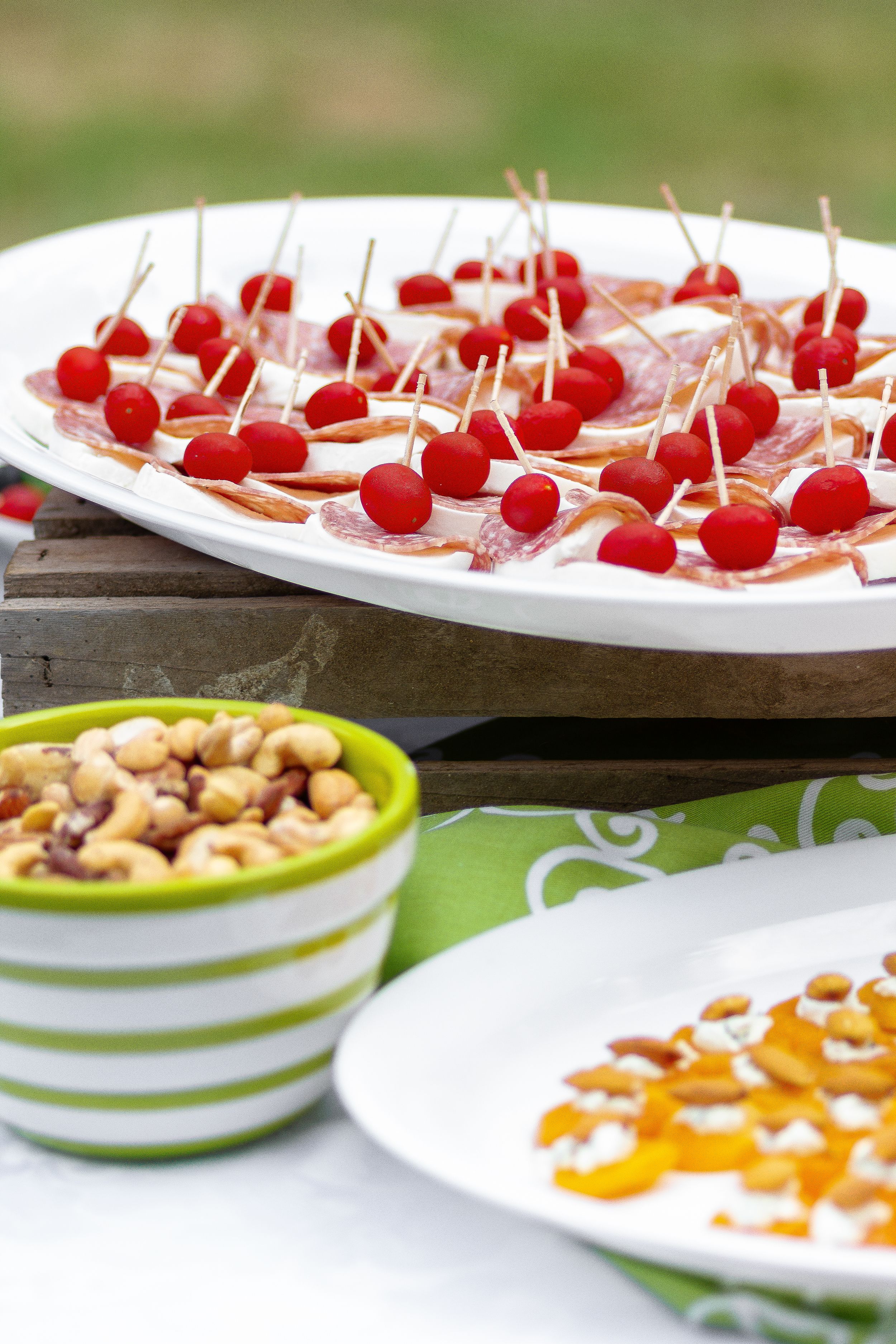 Platter of cherry tomato appetizers with mixed nuts and dips served outdoors.