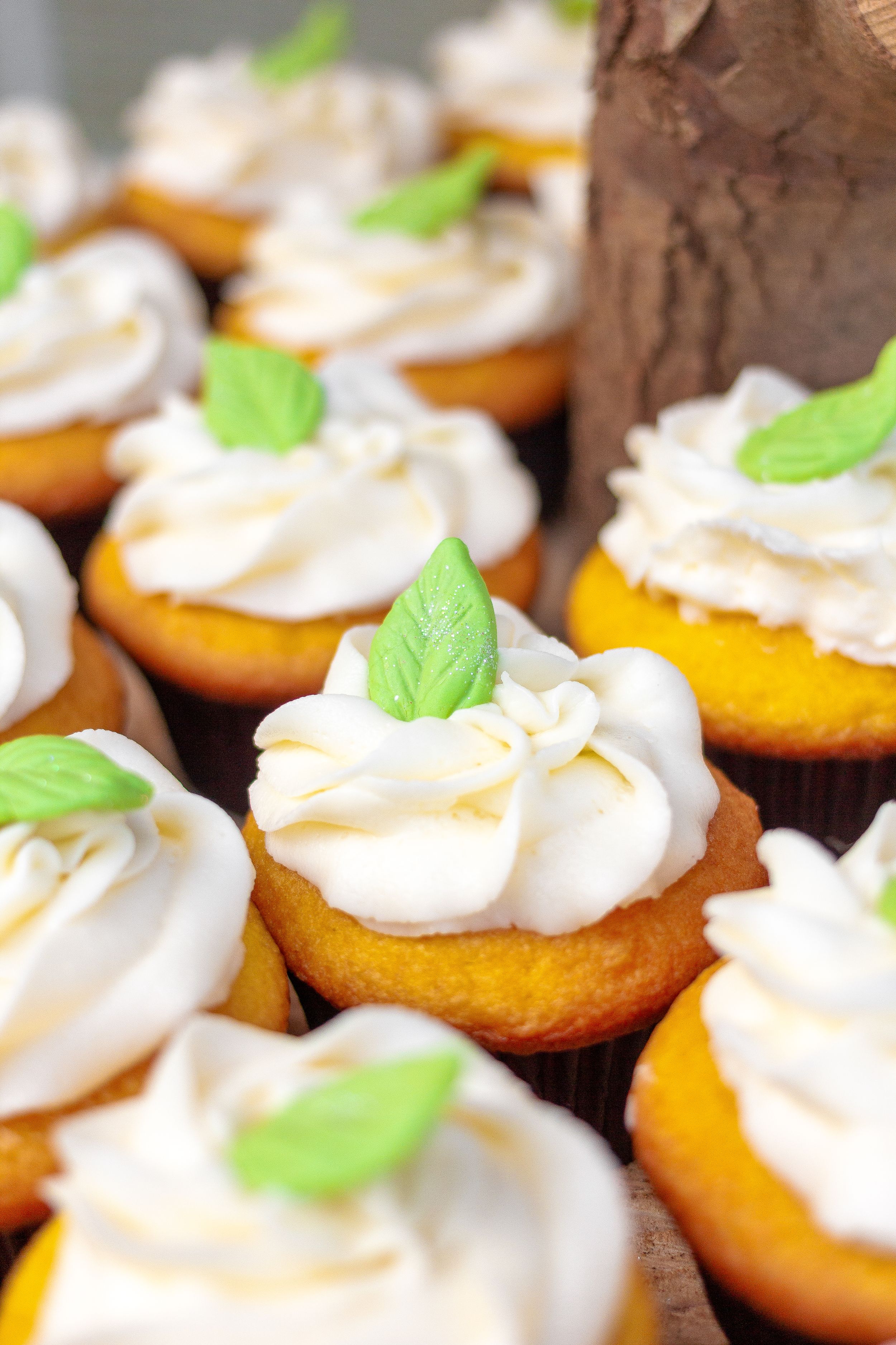 Yellow cupcakes topped with white frosting and fresh green basil leaves.