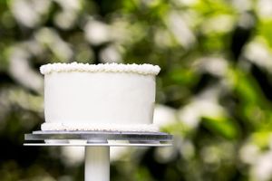 Simple white wedding cake on silver stand against blurred green background.