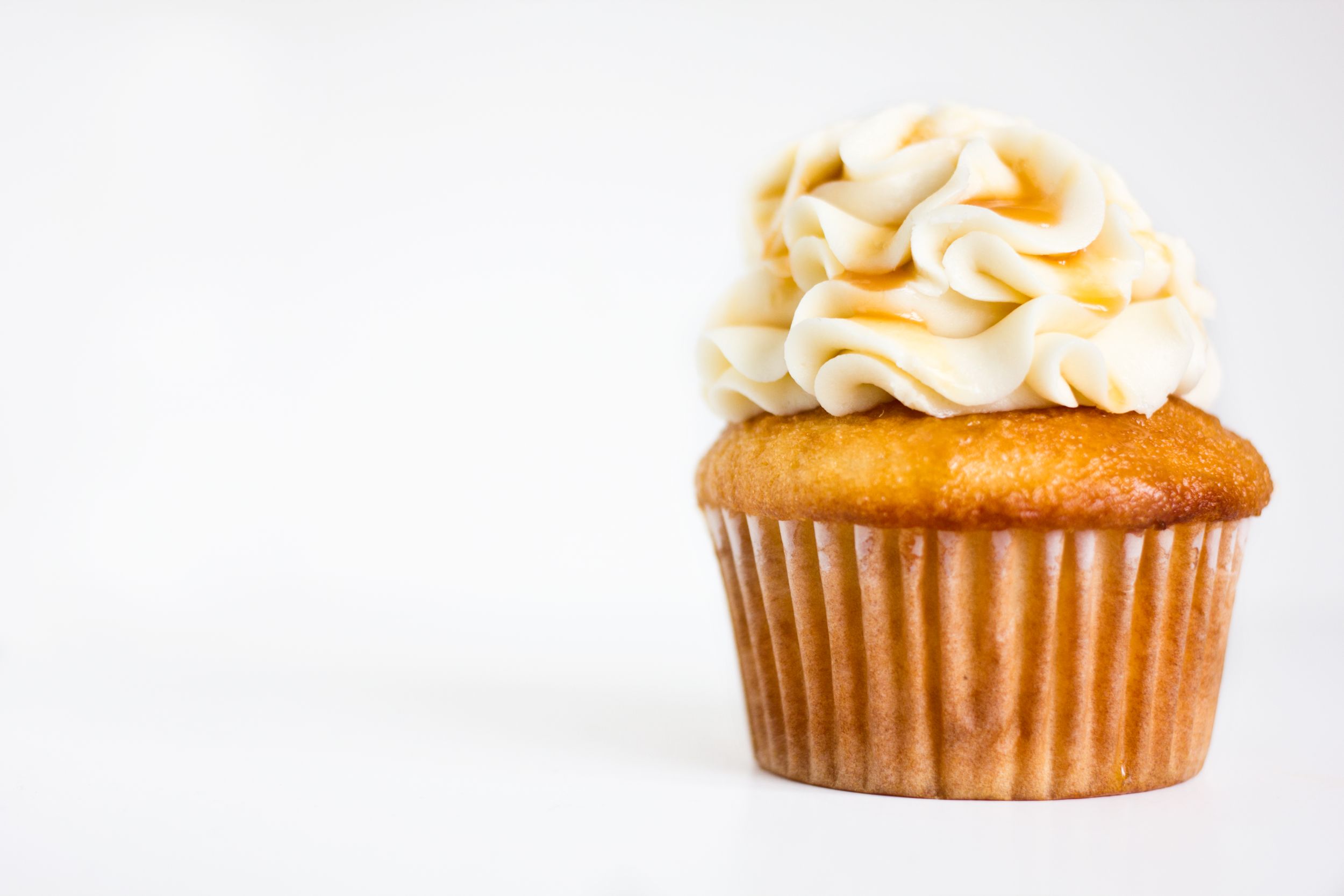 Golden vanilla cupcake with swirled buttercream frosting on white background.