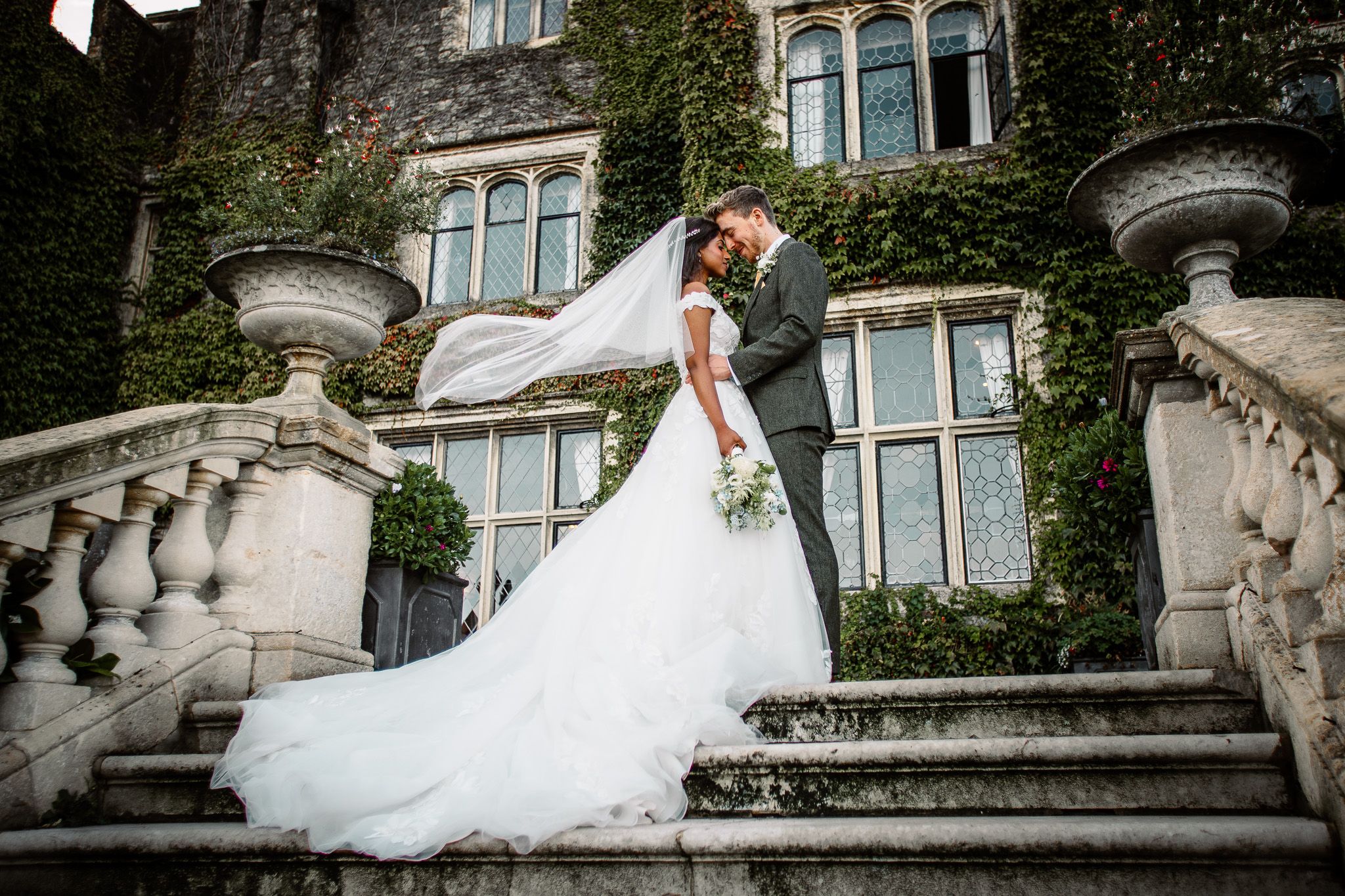 Wedding dress flowing against ivy-covered historic building with ornate architecture.