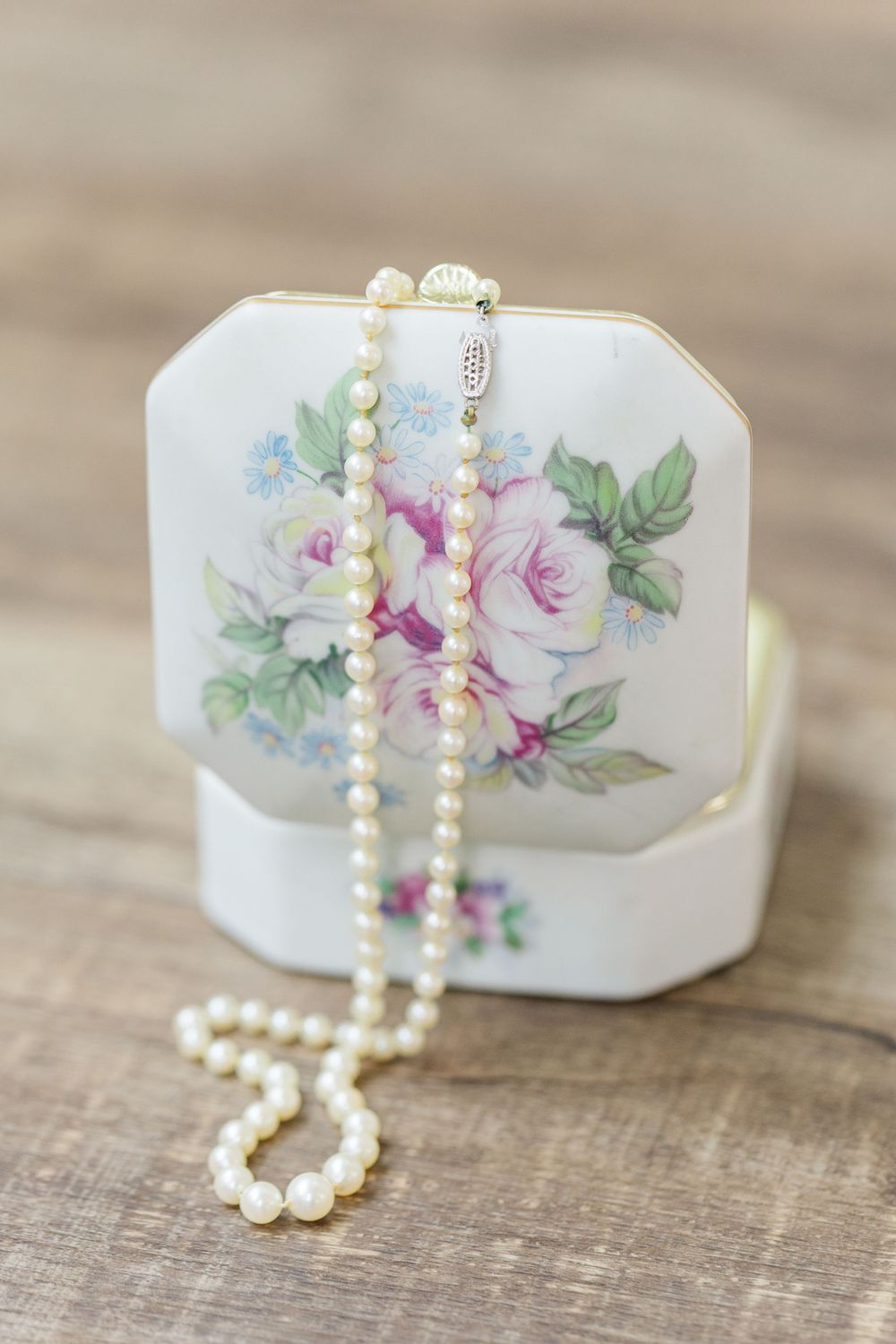 Delicate pearl necklace draped over a vintage floral ceramic trinket box.