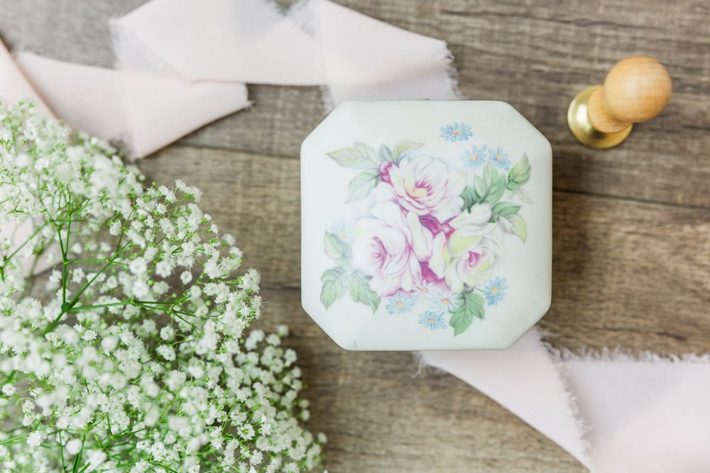 Vintage-style ring box with painted roses sits beside delicate baby's breath flowers.
