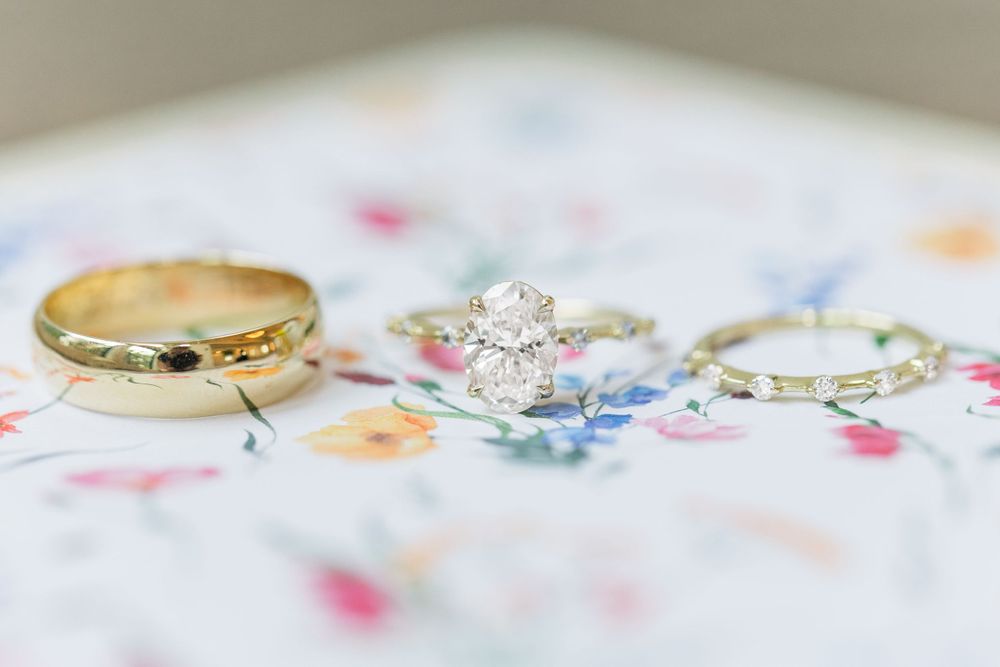 Wedding rings photographed on a floral patterned fabric, featuring gold band and diamond engagement ring.
