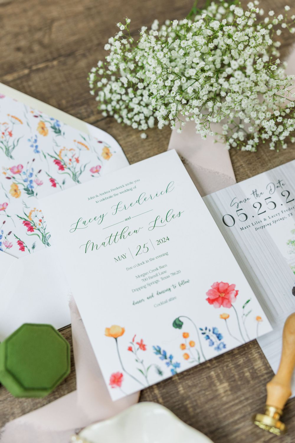 Floral wedding invitation with baby's breath bouquet and wax seal on wooden surface.