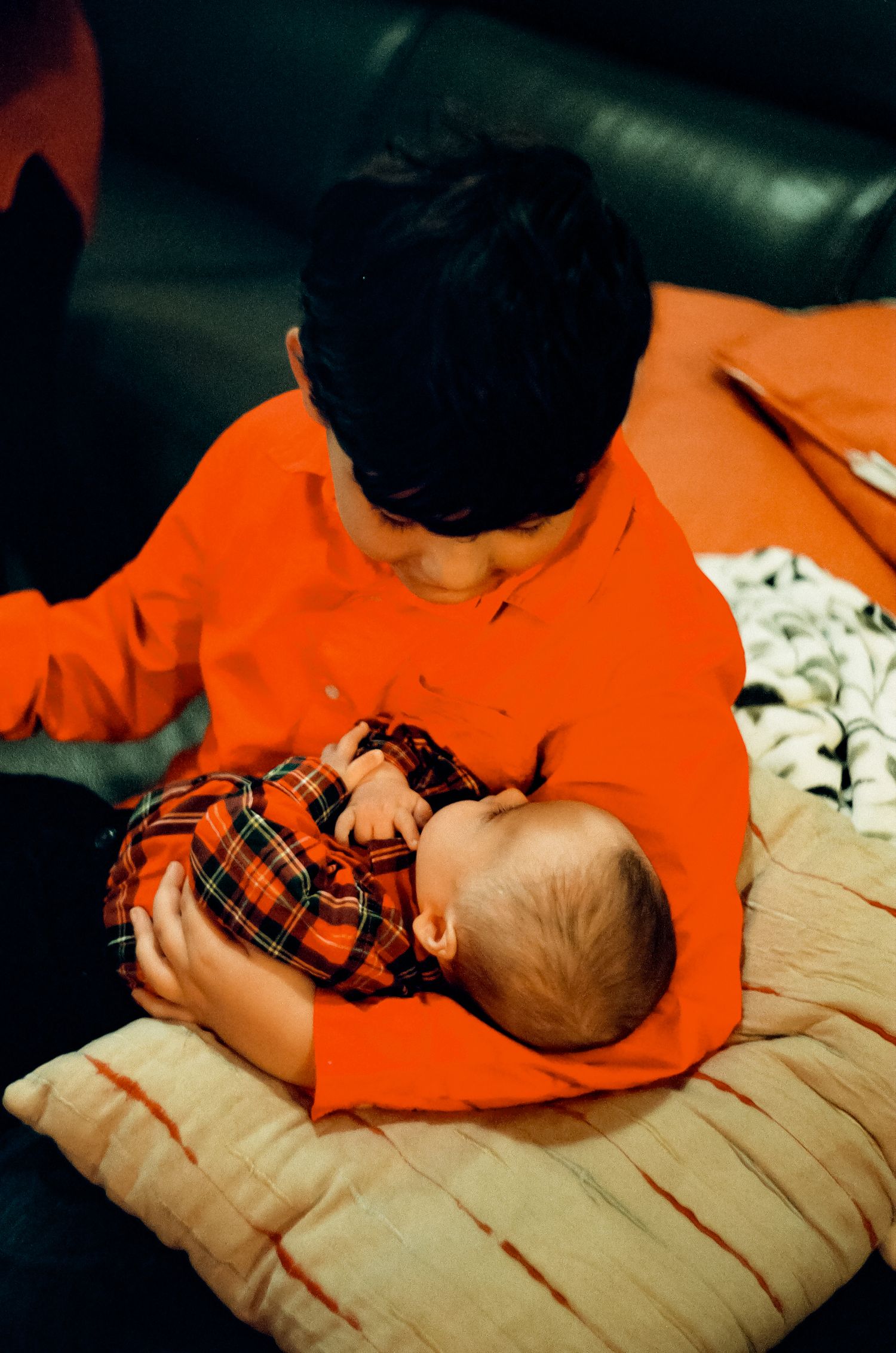 Person in orange sweater holding sleeping baby on striped pillow.