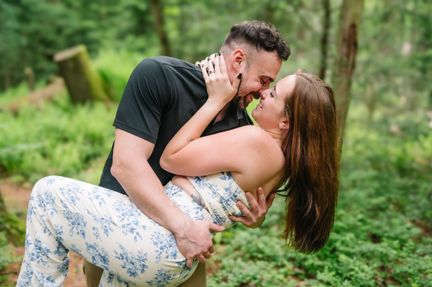 A romantic couple embraces and shares a tender moment together in a lush green forest setting.