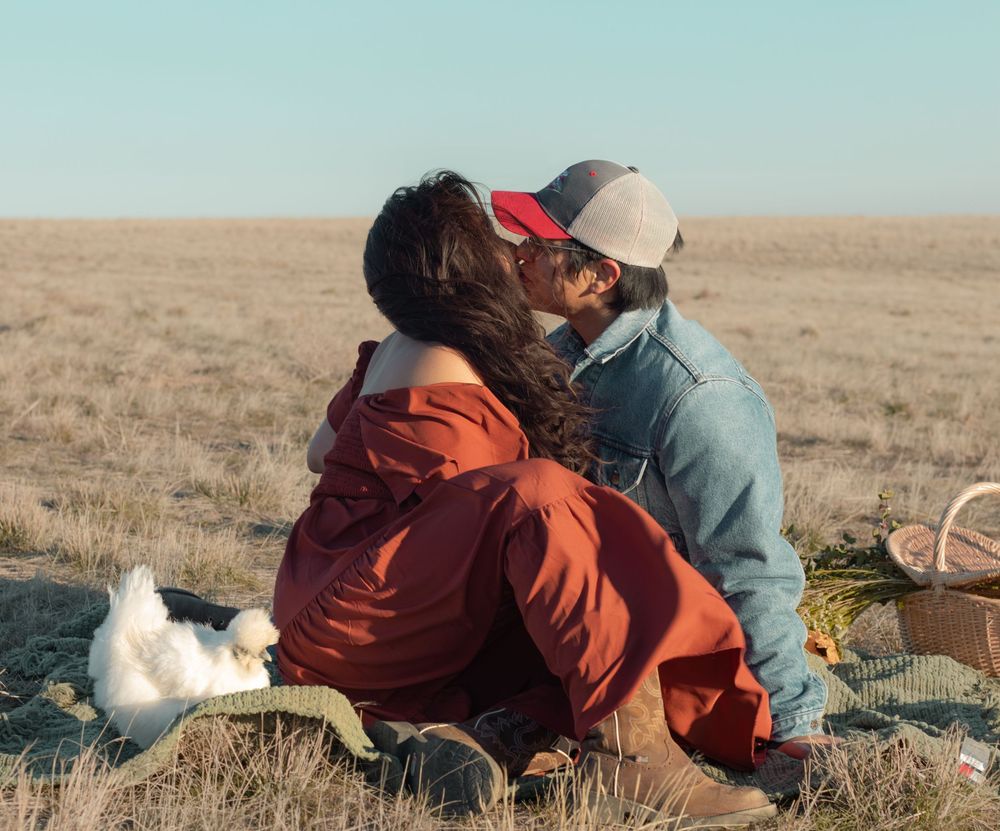Couple sharing a kiss while their goat stands next to them during cozy outdoor farm photo session