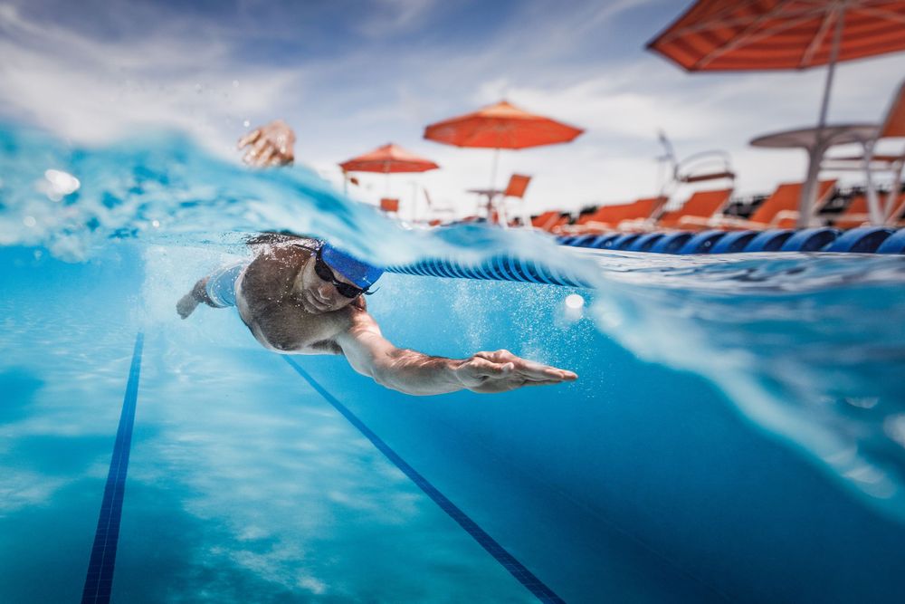 Underwater view of a swimmer gliding through a pool with orange umbrellas visible above the surface.