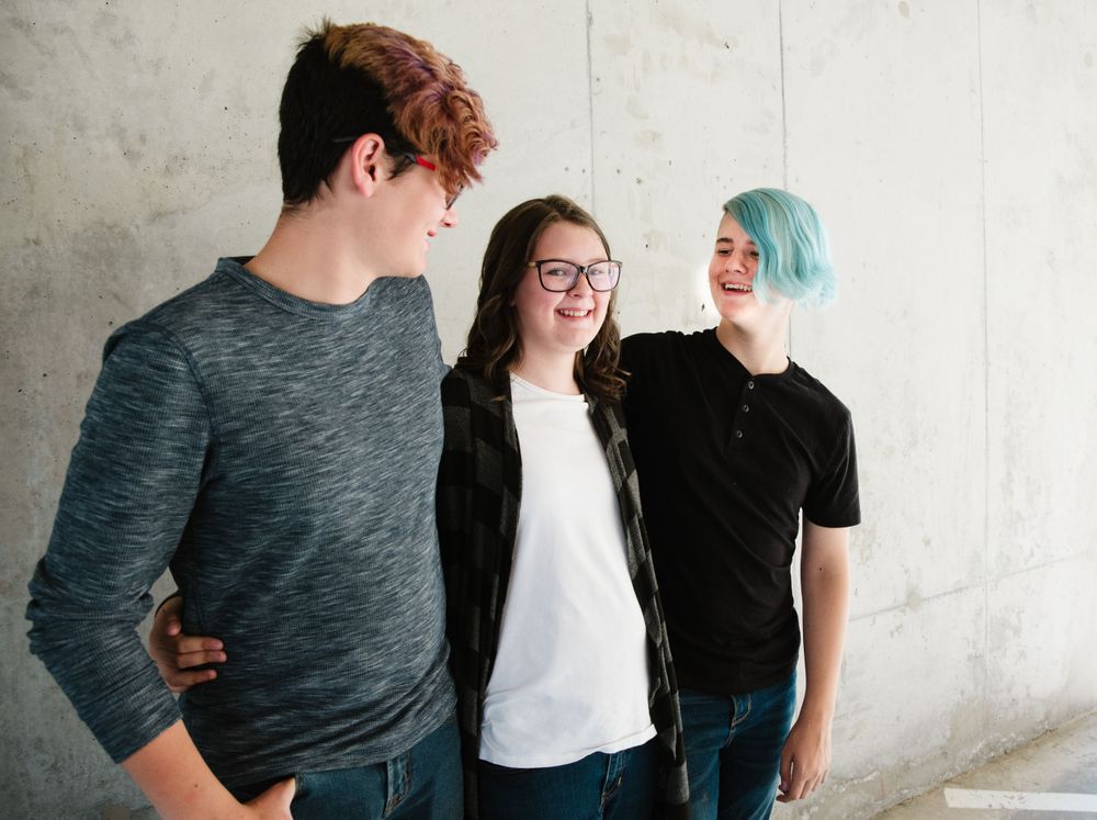 Group of friends with colorful hair posing casually against white wall in casual attire.