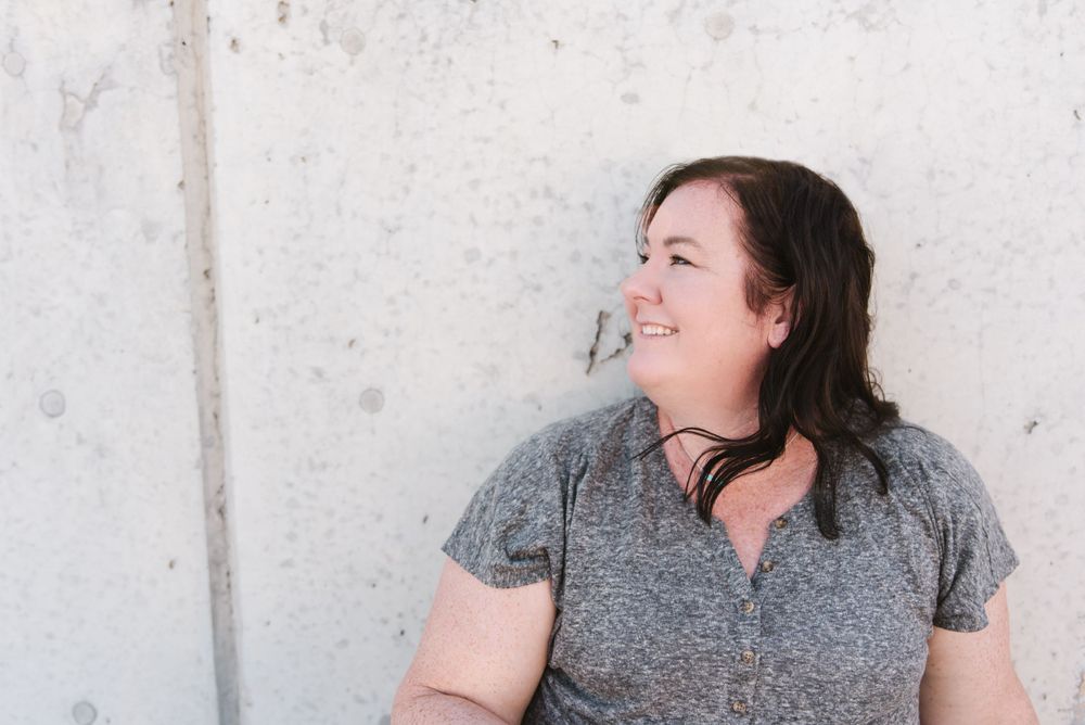 Person in grey shirt laughing joyfully against white wall background.