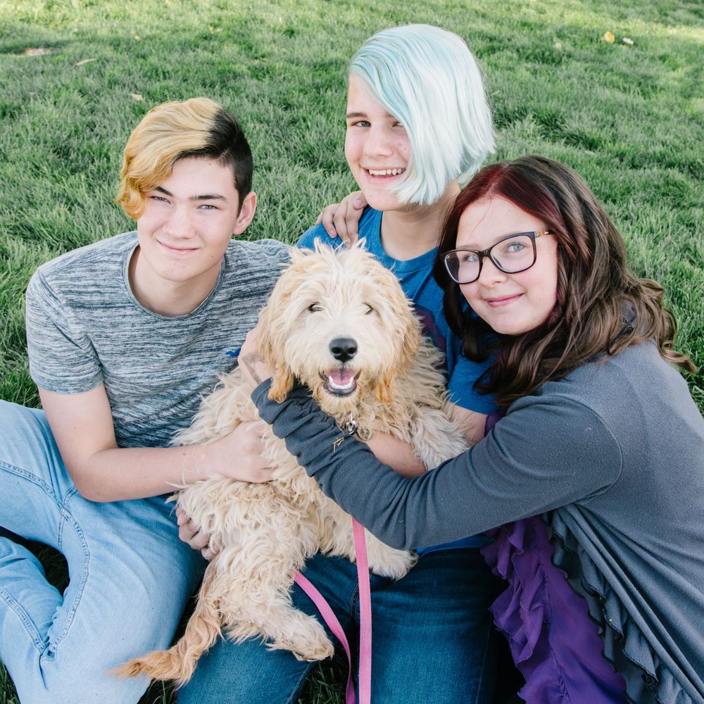 Group of friends and their golden doodle dog posing together on grass.
