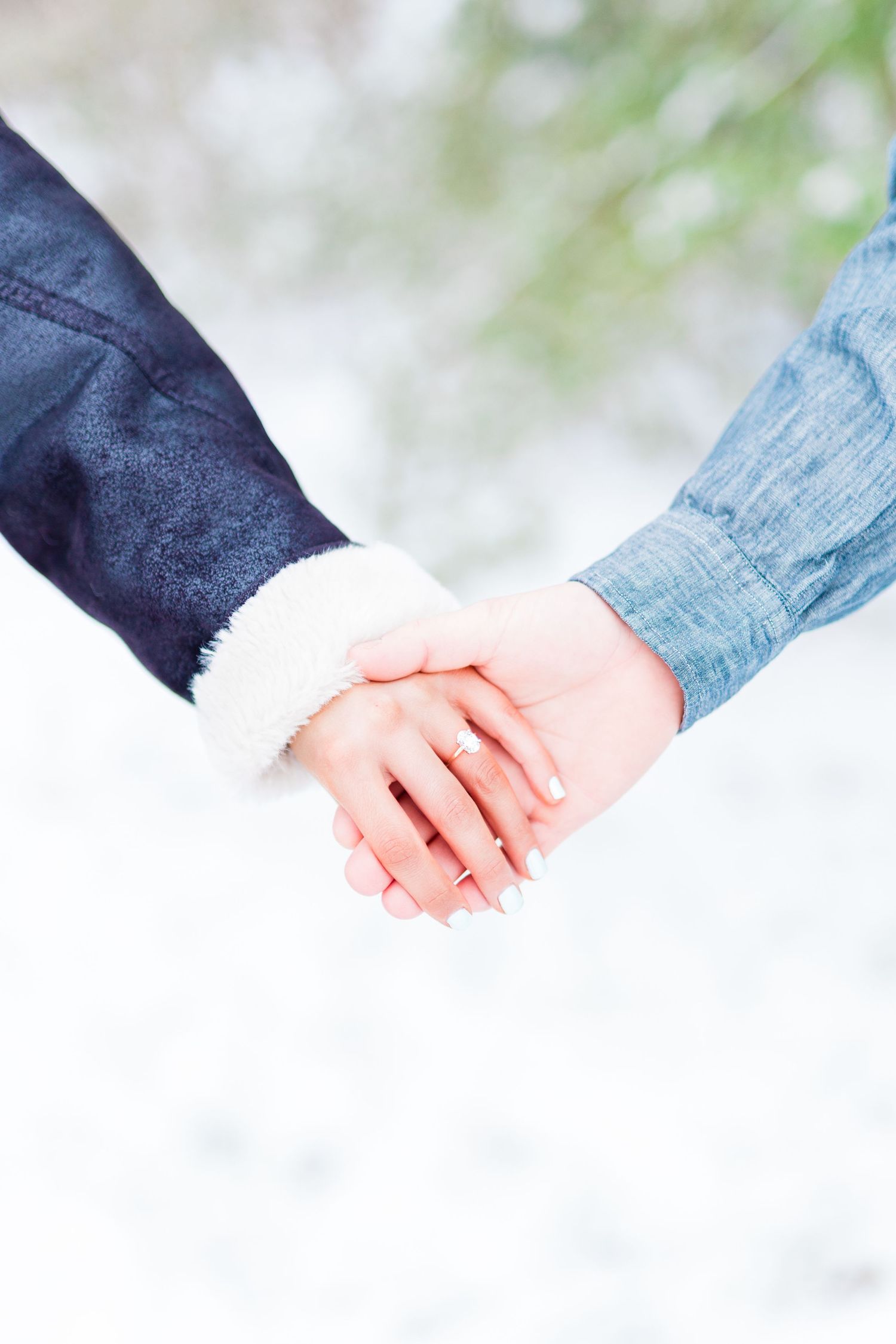 Two hands tenderly clasping together in winter against a soft blurred background.