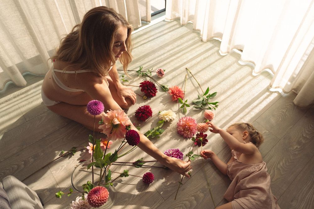 Two people sitting on the floor arranging pink and purple flowers in soft natural window light.