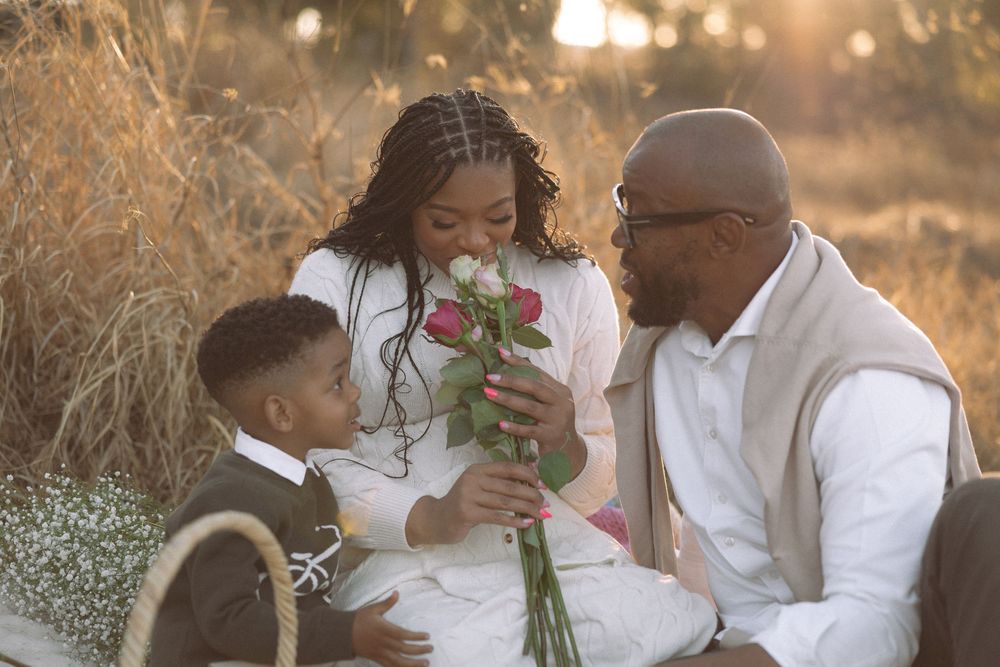 Romantic outdoor photo session at golden hour with couple holding roses and embracing in soft sunlight.
