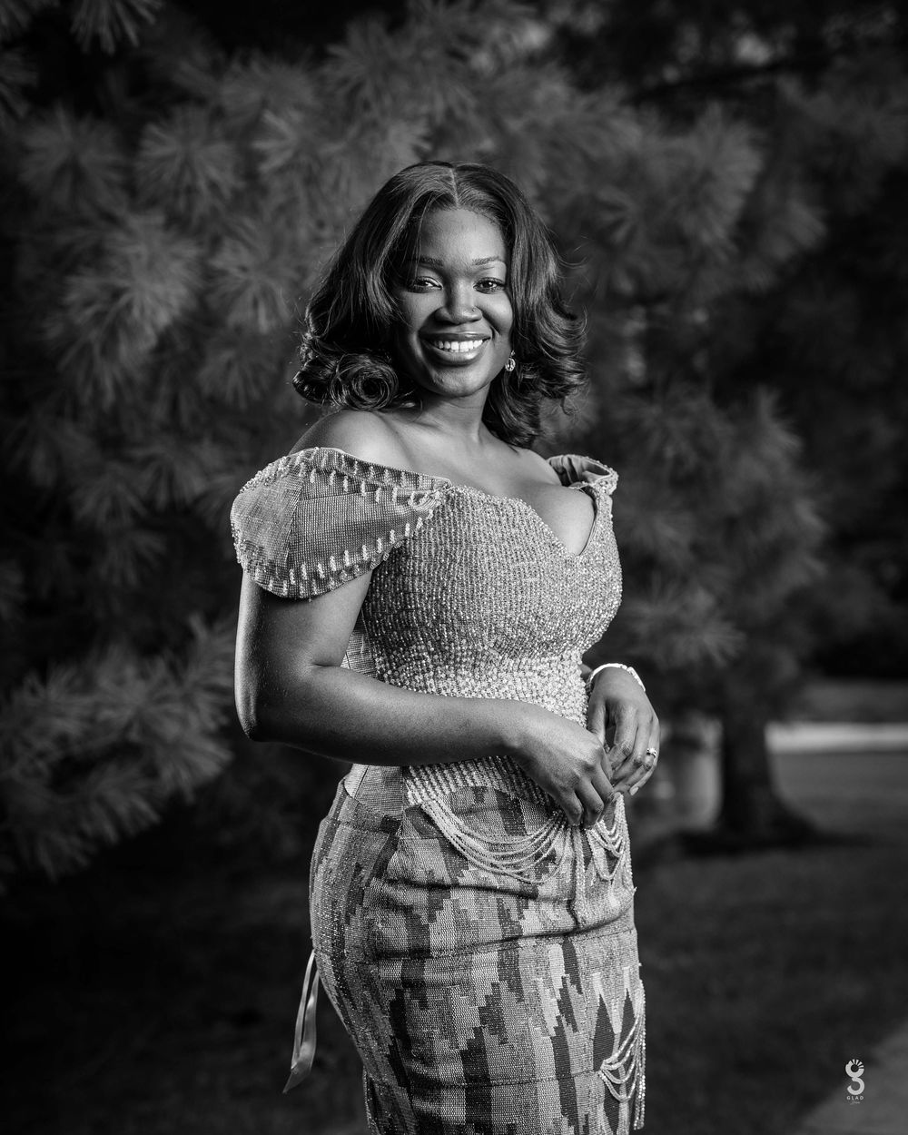 Black and white portrait of someone in an elegant beaded dress with cap sleeves standing outdoors against a blurred background.