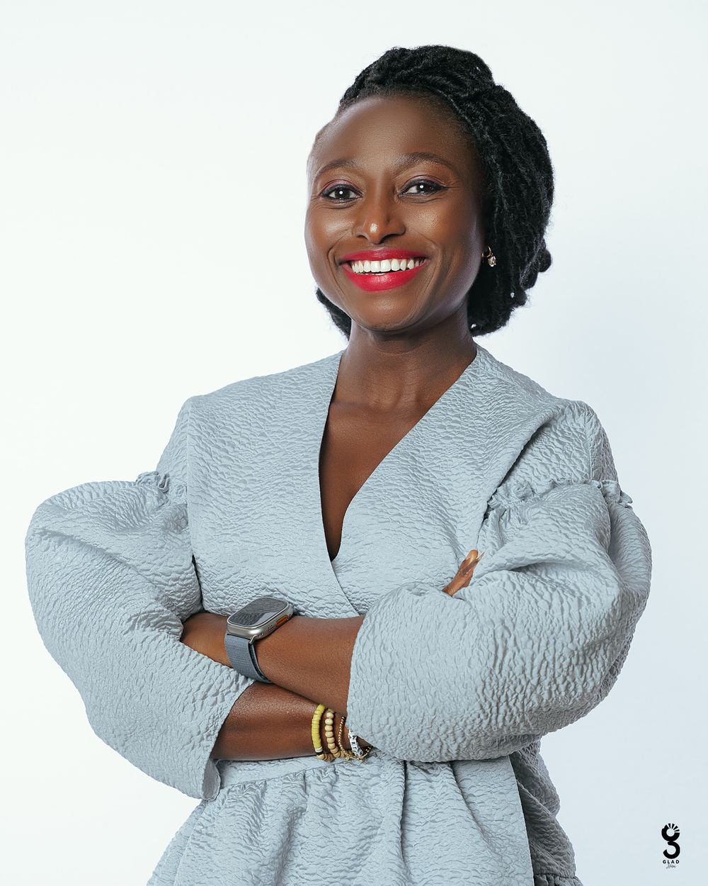 Professional studio portrait of someone in a stylish white textured blazer with gold bracelets and bright red lipstick.