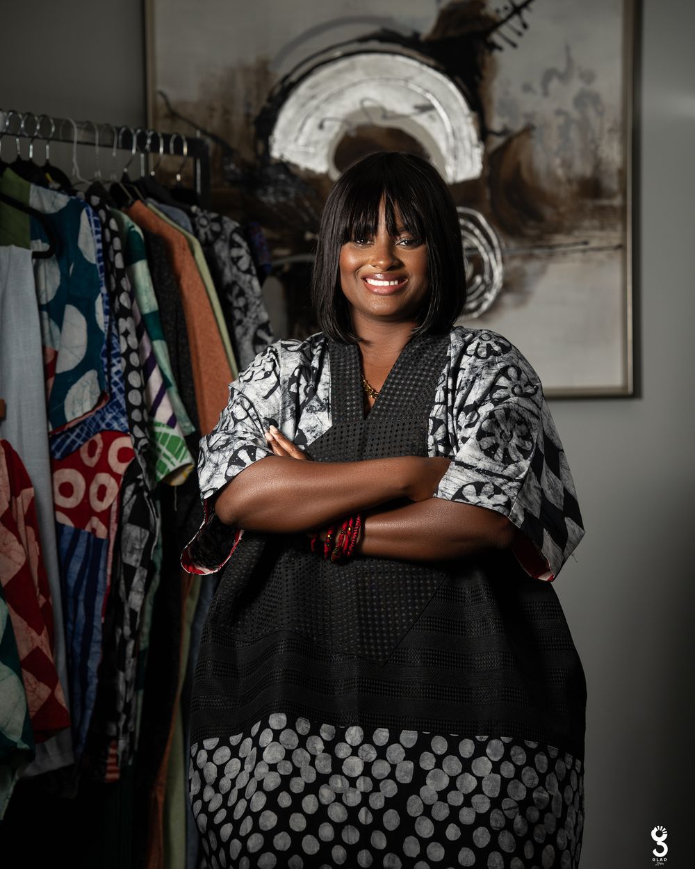 A person in a black and white polka dot dress stands in front of a clothing rack displaying colorful garments.