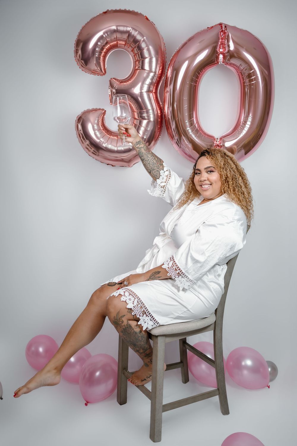 Large rose gold foil number 30 balloons with pink balloons decorate a studio setting for a milestone birthday photoshoot.