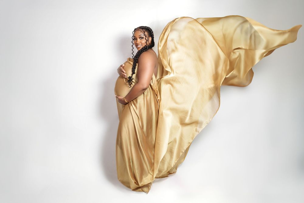 A glamorous figure poses in a flowing golden silk gown against a white background in an artistic fashion shot.