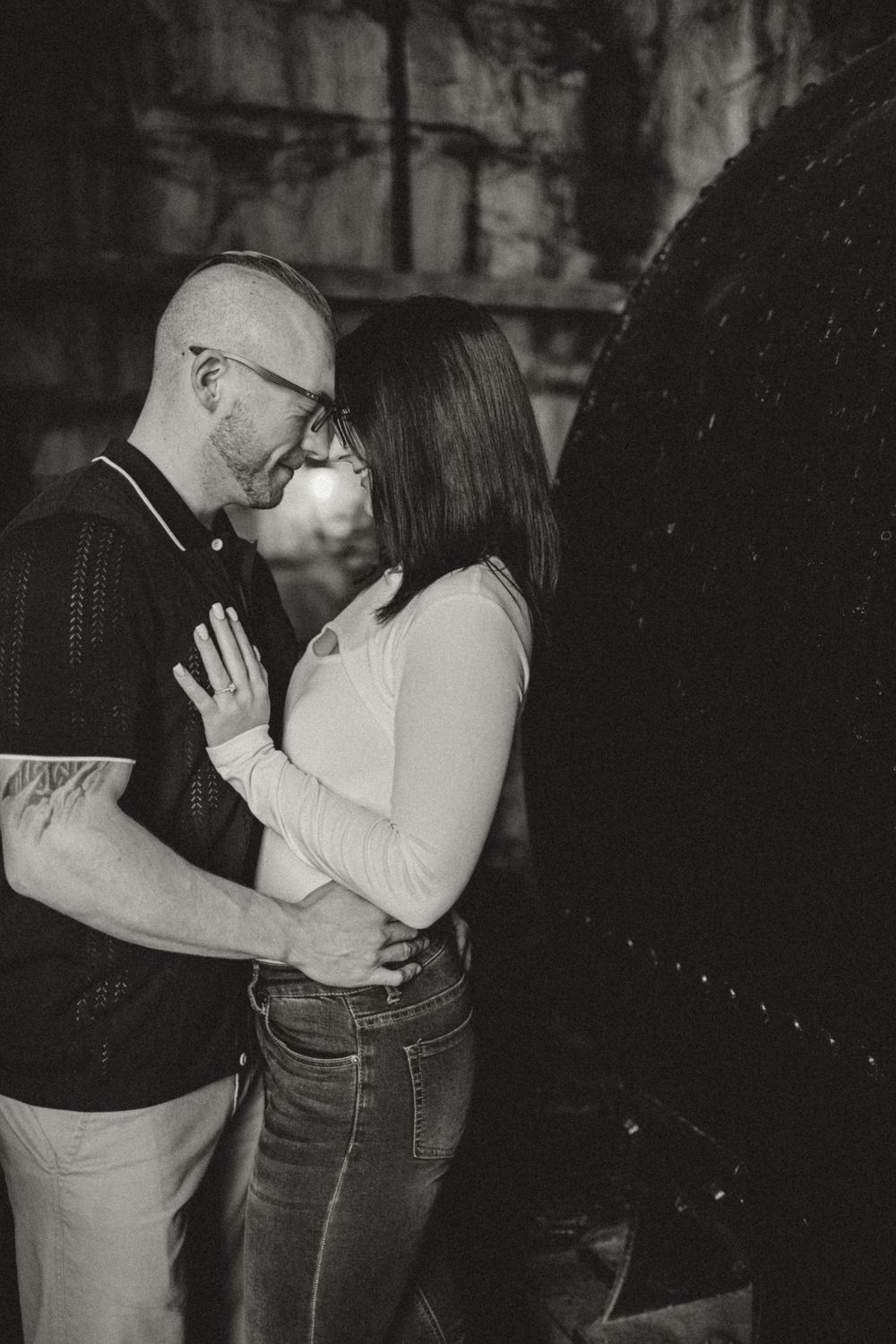 A couple shares an intimate romantic moment in black and white photography against an urban backdrop.