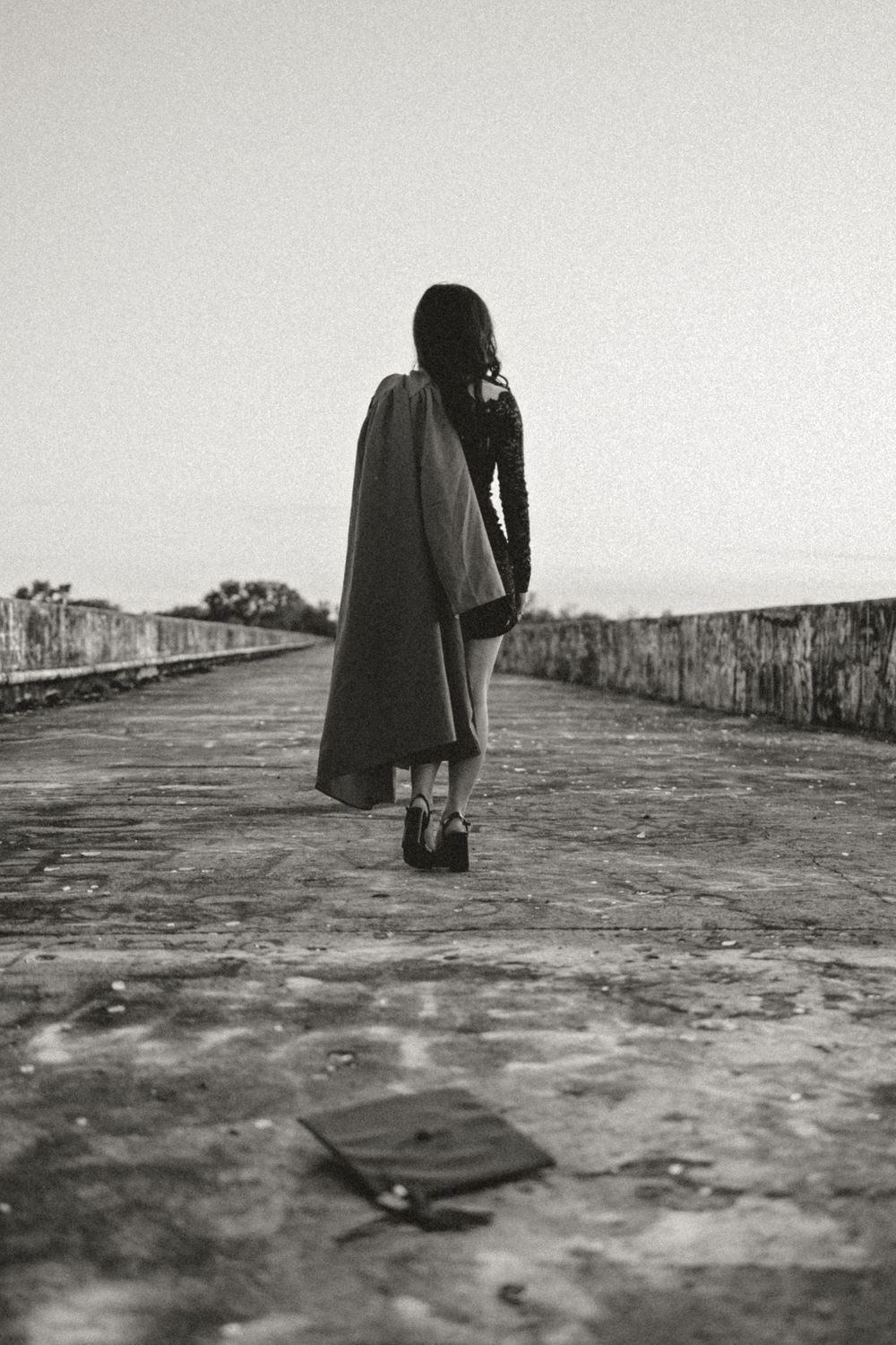 A black and white photo of a solitary figure in a coat standing on a stone walkway against a stark sky.