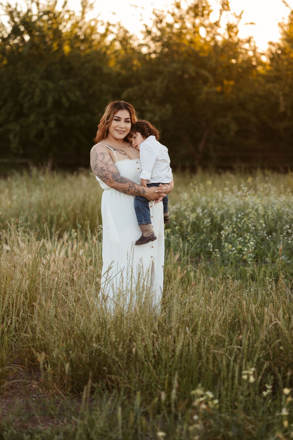 A parent and child share a tender moment in a sunlit meadow at golden hour, surrounded by tall grass and wildflowers.