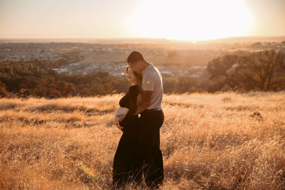 A park ranger stands in golden grass at sunset overlooking a scenic valley landscape.