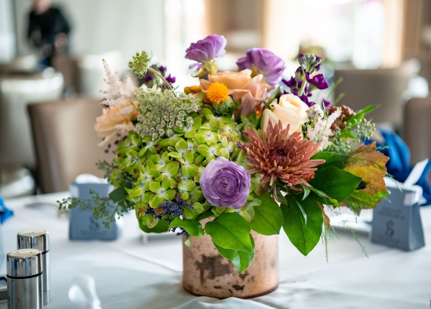 Beautiful centerpiece with purple roses, green hydrangeas and mixed flowers in a copper vase.
