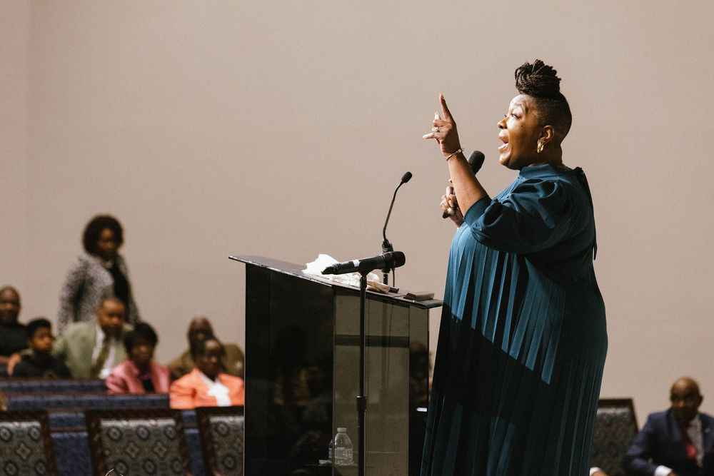 A speaker gestures passionately while delivering a speech at a podium wearing a flowing blue robe during a church service.