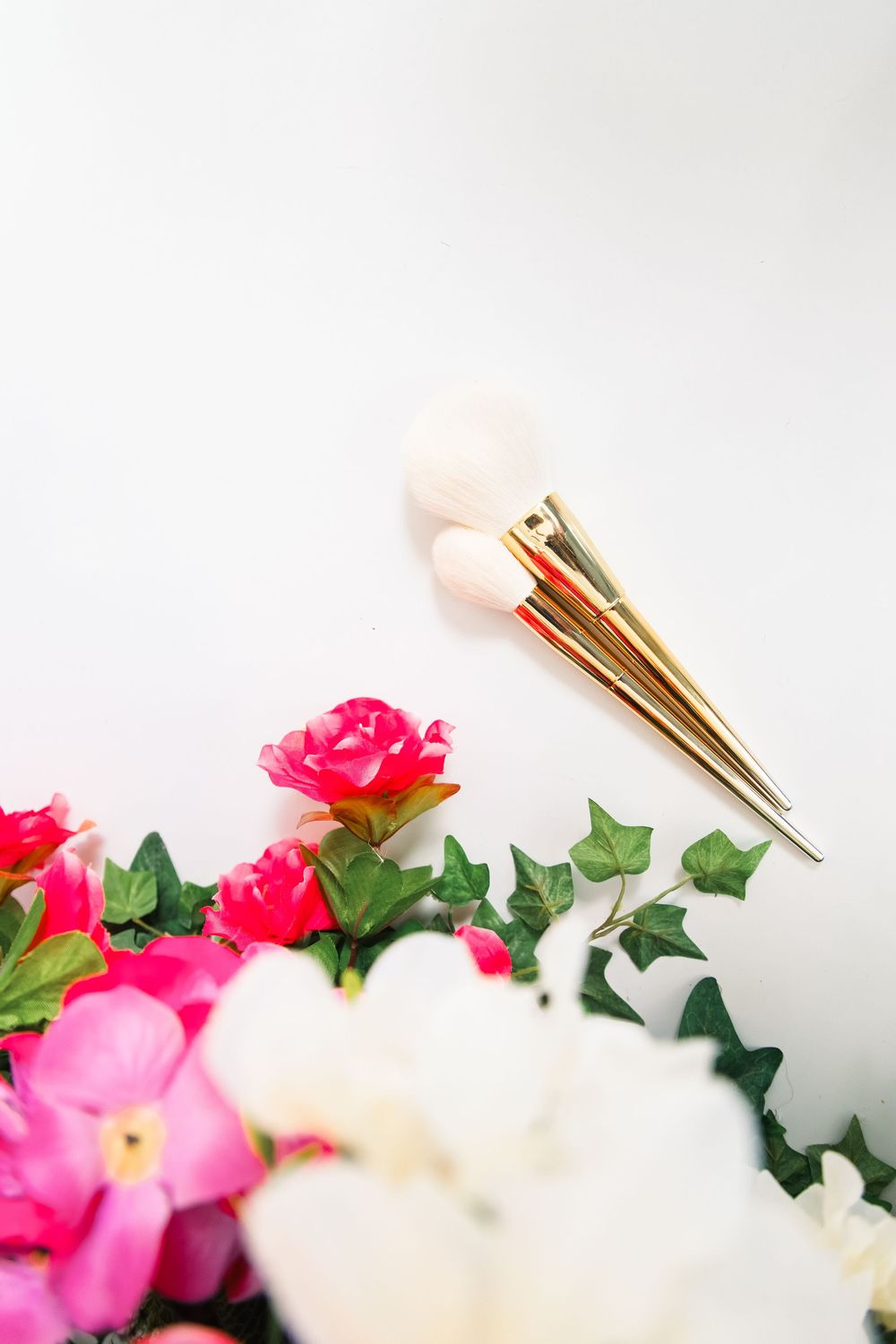 White and pink roses with green leaves arranged with gold-colored clothespins against a light gray background.