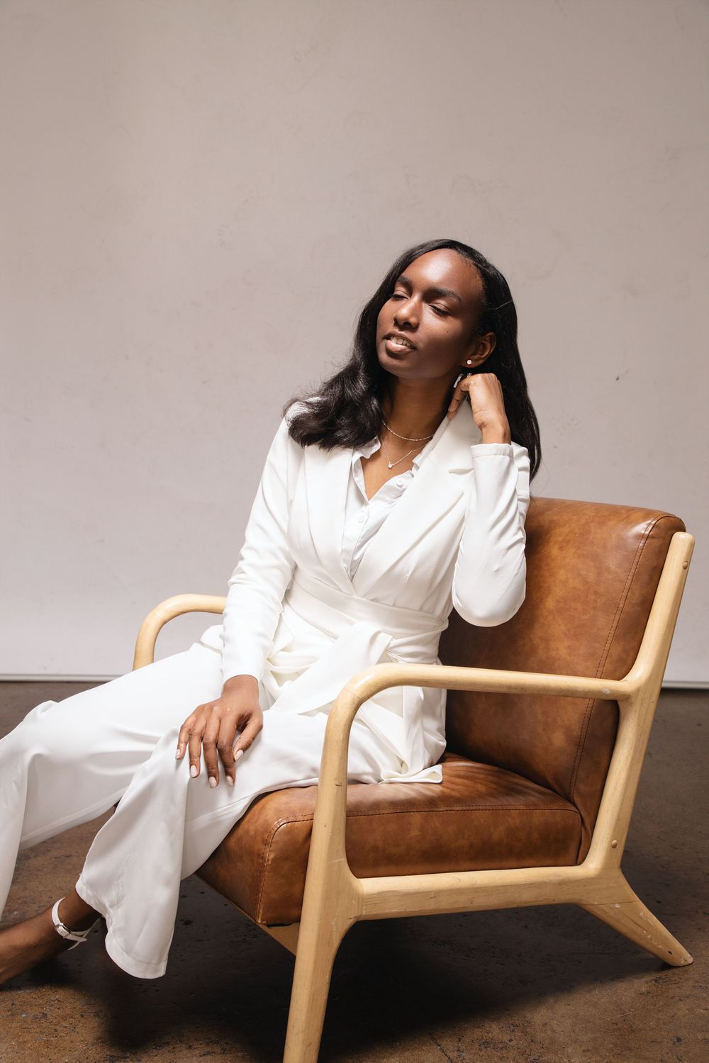 A relaxed figure in a white outfit reclines on a modern brown leather lounge chair, captured in different poses.