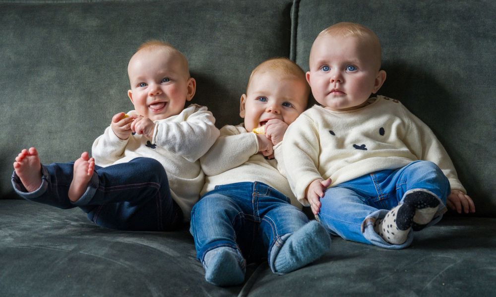 Drie vrolijke baby’s chillen samen op de bank in hun matching outfits.