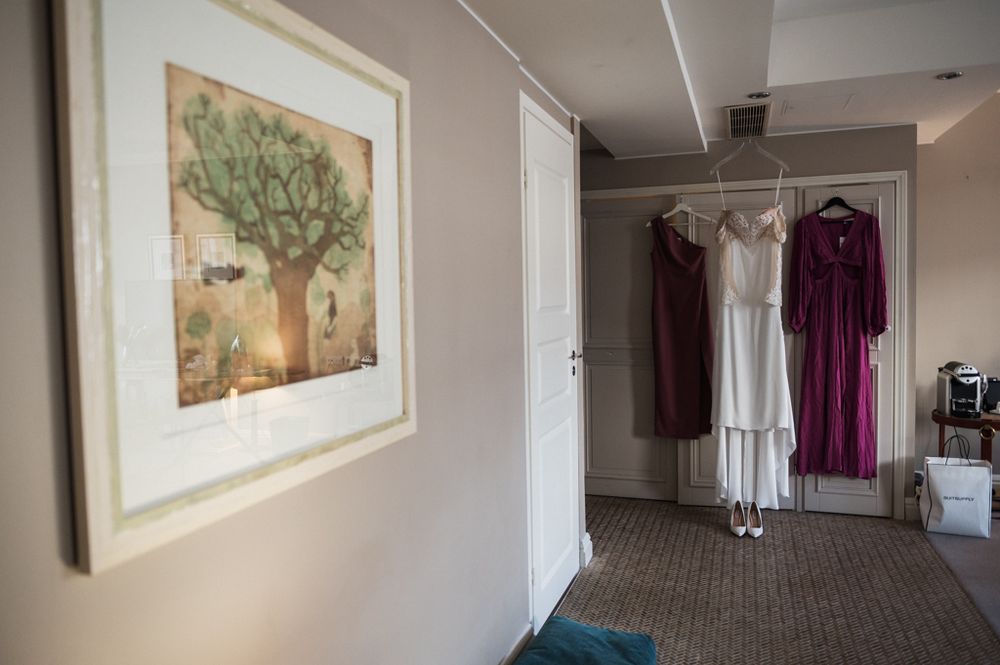 A framed tree artwork hangs on a wall next to dresses displayed on hangers in a dressing room.